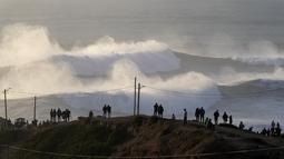 Orang-orang berdiri di atas tebing menyaksikan sesi selancar ombak besar di Praia do Norte, atau Pantai Utara, di Nazare, Portugal, Jumat (7/1/2022). Setiap tahunnya peselancar profesional menantang adrenalinnya mengarungi ombak besar dan tinggi di Pantai Praia do Norte. (AP Photo/Armando Franca)