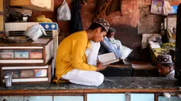 Seorang anak membaca Alquran di sebuah toko yang tutup selama bulan Ramadan saat penerapan lockdown di New Delhi, Senin (4/5/2020). Di emperan toko-toko yang tutup, umat muslim melaksanakan salat jemaah dengan menjaga jarak aman dan beberapa lainnya membaca kitab suci Alquran. (Sajjad HUSSAIN/AFP)