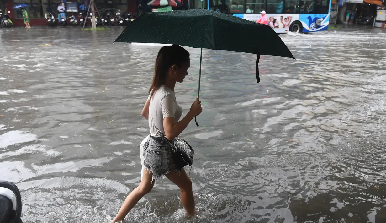 Seorang wanita melintasi banjir setelah badai tropis Talas terjadi di Hanoi, Vietnam utara (17/7). Menurut Direktur Pusat Peramalan Nasional Hidro-Meteorologi Badai Talas diprediksi akan melanda provinsi-provinsi utama Vietnam. (AFP Photo/Hoang Dinh Nam)