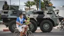 Seorang anak mengendarai sepeda saat tentara Maroko berpatroli di tengah wabah baru virus corona baru di kota Tangiers (11/8/2020). Tentara dikerahkan untuk meredam Lonjakan kasus Covid-19 di negara tersebut. (AFP/Fadel Senna)