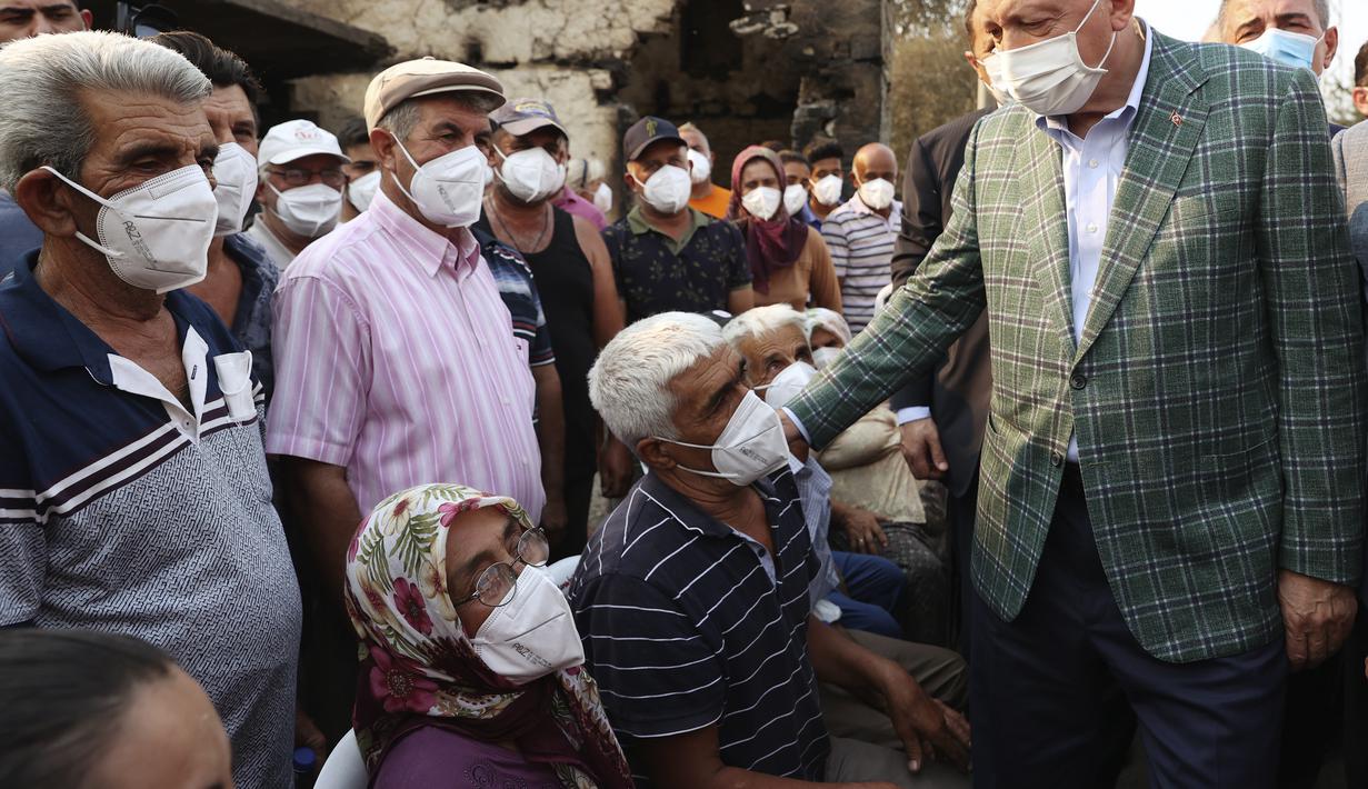 Presiden Turki Recep Tayyip Erdogan berbicara dengan penduduk desa di depan sebuah rumah yang hancur akibat kebakaran hutan di Manavgat, Antalya, Turki, Sabtu (31/7/2021). (Turkish Presidency via AP, Pool)
