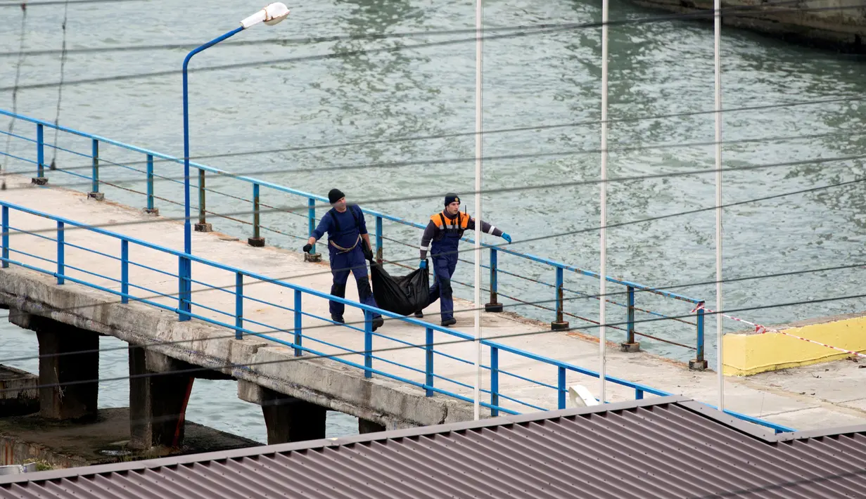 Petugas Kementerian Pertahanan Rusia membawa kantong plastik di dermaga Laut Hitam di pinggiran Sochi, Rusia (25/12). Pesawat tersebut tengah terbang menuju provinsi Latakia di Suriah. (REUTERS/Yevgeny Reutov)  