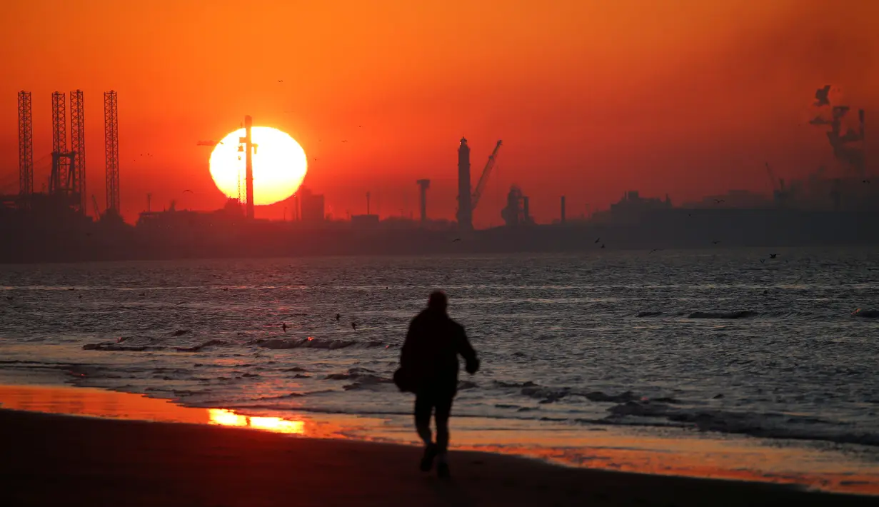Seorang pria berjalan di dekat Industri pelabuhan Dunkirk saat matahari terbenam di Leffrinckoucke, Prancis (25/2). (Reuters/Pascal Rossignol)