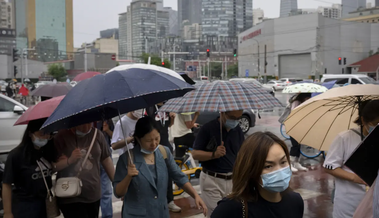 Komuter yang mengenakan masker berjalan melintasi persimpangan selama jam sibuk pagi hari pada hari hujan di Beijing, Rabu (29/6/2022). China memangkas lama karantina wajib bagi pelancong luar negeri dari 21 hari menjadi tujuh hari ditambah tiga lagi pemantauan di rumah. (AP Photo/Mark Schiefelbein)