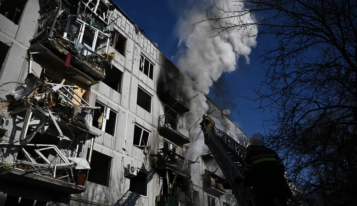 Petugas berusaha memadamkan kebakaran pada sebuah gedung setelah pemboman di Kota Chuguiv, Ukraina timur, 24 Februari 2022. Angkatan bersenjata Rusia mencoba menyerang Ukraina dari beberapa arah, menggunakan sistem roket dan helikopter untuk menyerang posisi Ukraina di selatan. (Aris Messinis/AFP)