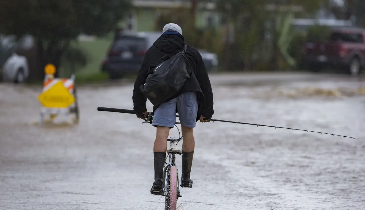Seorang pria mengendarai sepedanya melewati banjir di College Road di Watsonville, California, Jumat, 10 Maret 2023. Lebih dari 9.000 penduduk California berada di bawah perintah evakuasi pada hari Jumat karena sungai atmosfer baru membawa hujan lebat, badai petir dan angin kencang, sungai meluap dan anak sungai dan membanjiri beberapa jalan raya utama selama perjalanan pagi. (AP Photo/Nic Coury)