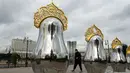 Seorang wanita berjalan melewati "benda seni Matryoshki", tujuh boneka bersarang tradisional Rusia "matryoshka" yang dicerminkan dengan hiasan kepala "kokoshnik", dengan gedung Pemerintah Rusia terlihat di latar belakang, di pusat kota Moskow (9/9/2021).  (AFP/Kirill Kudryavtsev)