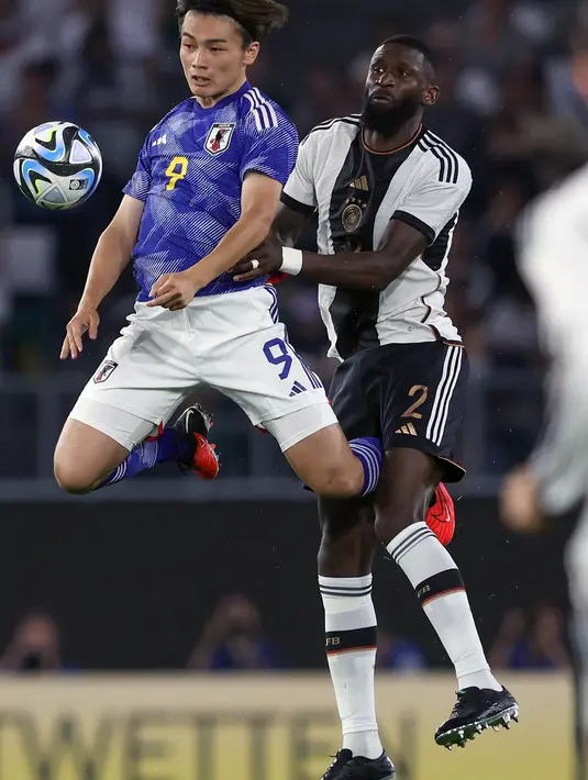 Penyerang Jepang #09 Ayase Ueda (Kiri) dan bek Jerman #02 Antonio Ruediger berebut bola pada laga uji coba internasional di Stadion Volkswagen Arena, Minggu (10/9/2023) dini hari WIB. (Photo by Ronny HARTMANN / AFP)
