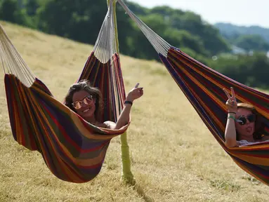 Dua wanita bersantai di tempat tidur gantung saat menghadiri Festival Musik Glastonbury di Worthy Farm, di Somerset, Inggris, (22/6). Festival Glastonbury merupakan festival musik paling populer di dunia. (AFP Photo/Oli Scarff)