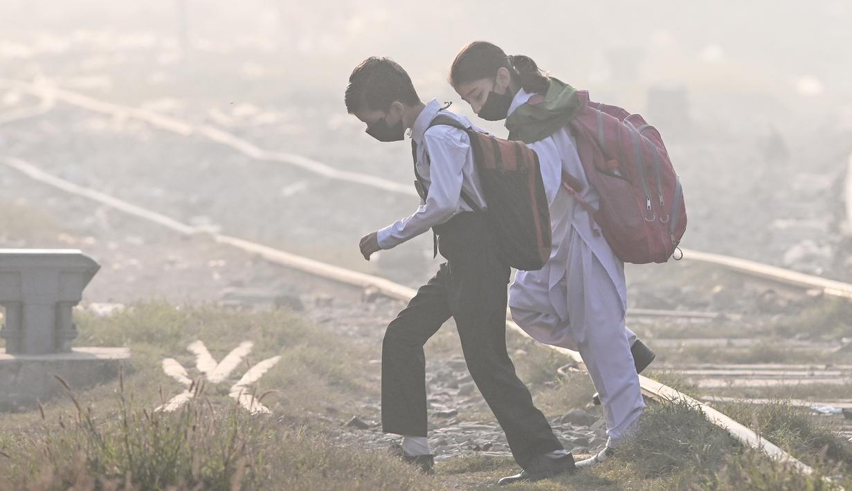 Anak-anak sekolah mengenakan masker berjalan melintasi rel kereta api di tengah kabut asap tebal di Lahore, Pakistan pada Rabu 20 November 2024. (Arif ALI/AFP)