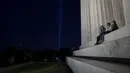 Orang-orang duduk di tangga Lincoln Memorial saat penghormatan 'Menara Cahaya' naik ke angkasa dari dekat Pentagon pada malam peringatan 20 tahun 9/11 di Washington, DC. (10/9/2021). (Anna Moneymaker/Getty Images/AFP)