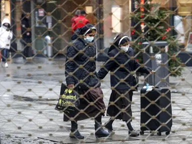 Dua biarawati terlihat berjalan dari balik pagar besi pusat perbelanjaan di Essen, Jerman, Senin (14/12/2020). Jerman melakukan lockdown nasional pada 16 Desember 2020 untuk memerangi pandemi COVID-19. (AP Photo/Martin Meissner)