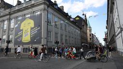 Pengendara sepeda dan pejalan kaki melewati poster raksasa yang mengumumkan balapan sepeda Tour de France 2022 Grand Depart di Kopenhagen, Denmark pada 28 Juni 2022. Nuansa kuning menyambut kejuaraan balap sepeda legendaris, Tour de France (TdF), yang pada edisi 2022 akan bermula dari Kopenhagen. (Thomas SAMSON / AFP)