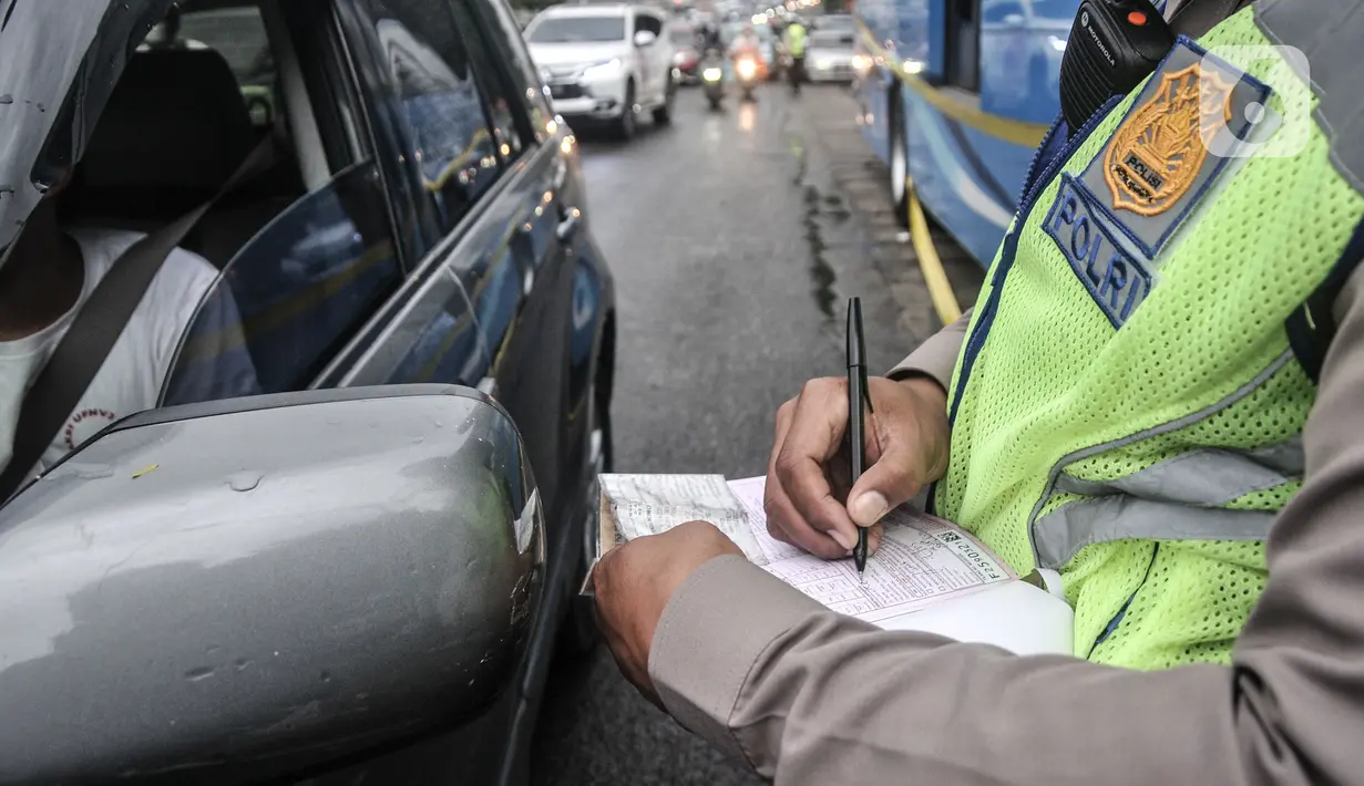 Petugas kepolisian menilang pengendara mobil yang melanggar aturan ganjil genap di Jalan MT Haryono, Jakarta, Kamis (28/10/2021). Para pelanggar sistem ganjil genap dikenakan sanksi tilang berupa denda maksimal Rp500 ribu. (merdeka.com/Iqbal S Nugroho)