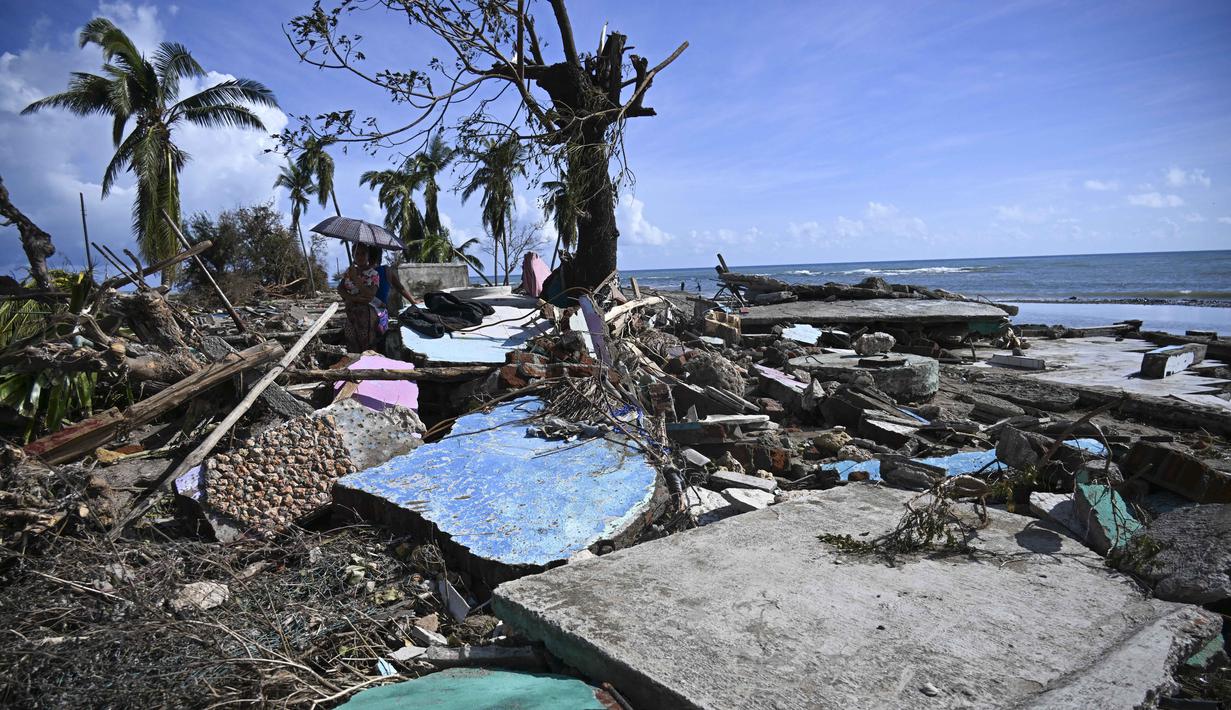 Sepasang suami istri berjalan di tengah puing-puing rumah yang rusak akibat Badai Melissa di desa Boca de Dos Rios, provinsi Santiago de Cuba, Kuba pada Kamis 30 Oktober 2025. Badai Melissa bergerak menuju Bermuda setelah menghancurkan Karibia dan menewaskan sedikitnya 20 orang di Haiti, serta menghancurkan sebagian Jamaika dan Kuba. (YAMIL LAGE/AFP)