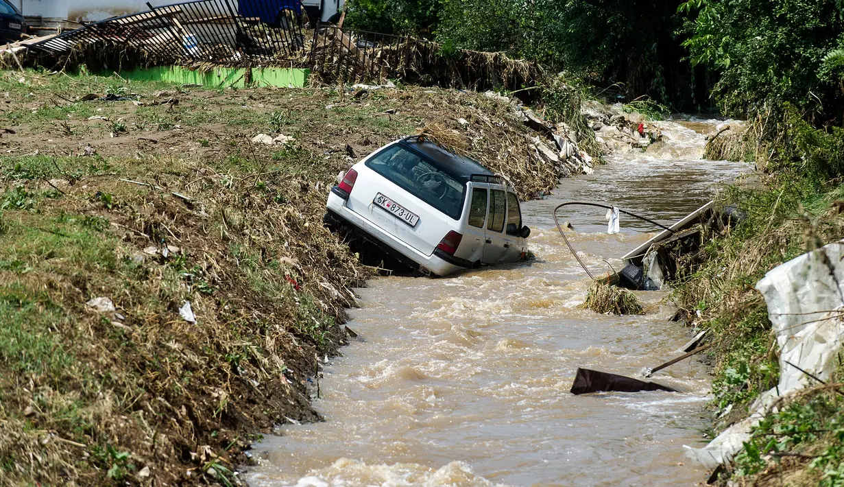 Mobil masuk ke sebuah kanal akibat banjir bandang di Ibu Kota Skopje, Makedonia, Minggu (7/8). Pemerintah menyatakan keadaan darurat sehari setelah setidaknya 21 orang tewas dalam banjir bandang yang disebabkan badai. (Robert ATANASOVSKI/AFP)