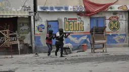 Petugas polisi berlindung selama operasi anti-geng di lingkungan Portail, Port-au-Prince, sehari setelah massa di ibu kota Haiti itu menarik 13 tersangka anggota geng dari tahanan polisi lalu memukuli dan membakar mereka sampai mati. (AP Photo/Odelyn Joseph)