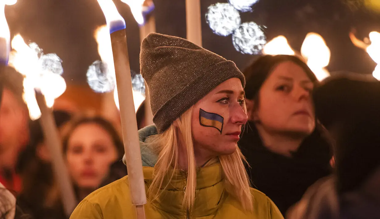 Seorang wanita memegang obor saat demonstrasi untuk Ukraina yang diselenggarakan oleh Greenpeace di Heroes Square, Budapest, Hungaria, 9 Maret 2022. Invasi Rusia ke Ukraina telah memicu migrasi massal terbesar di Eropa dalam beberapa dekade. (AP Photo/Anna Szilagyi)