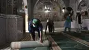 Umat Muslim menggulung karpet sajadah dari aula utama masjid menyusul pembatasan baru pemerintah baru menjelang bulan suci Ramadan di Rawalpindi, Pakistan, Senin (5/4/2021). Lantai masjid juga harus dibersihkan dengan larutan klorin dalam air. (Aamir QURESHI/AFP)