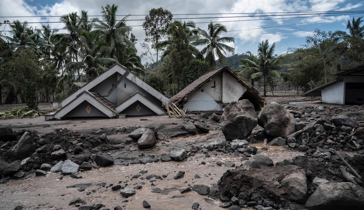 Batu-batu besar tersebar di depan rumah-rumah yang rusak di Dusun Kamar Kajang, Lumajang, Kamis (9/12/2021). Luapan air sungai bercampur material lahar dingin erupsi Gunung Semeru merendam puluhan rumah akibat diguyur hujan deras pada Selasa (7/12) dan Rabu (8/12) malam. (Juni Kriswanto/AFP)