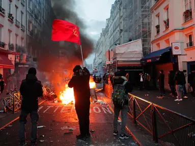 Seorang anggota komunitas Kurdi mengibarkan bendera komunis Kurdi dekat barikade yang terbakar di TKP tempat terjadinya penembakan di Paris, Prancis, 23 Desember 2022. Demonstrasi memprotes penembakan komunitas suku Kurdi di Paris berujung rusuh. (AP Photo/Lewis Joly)