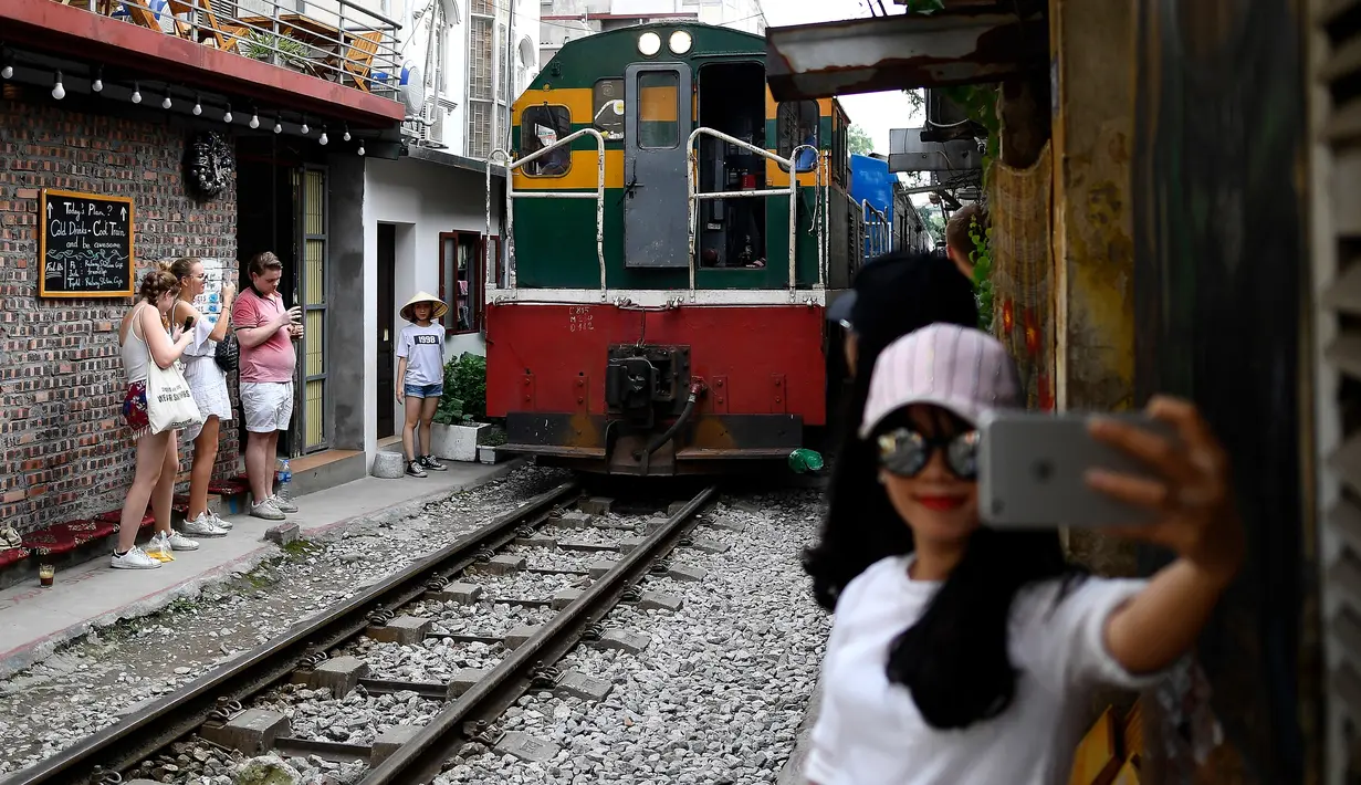 Foto pada 8 Juni 2019 menunjukkan seorang wanita berswafoto saat sebuah kereta melintasi jalur kereta api populer di Hanoi. Di ibu kota Vietnam tersebut rel-rel kereta yang berada di permukiman padat penduduk dijadikan destinasi wisata selfie. (Photo by Manan VATSYAYANA / AFP)