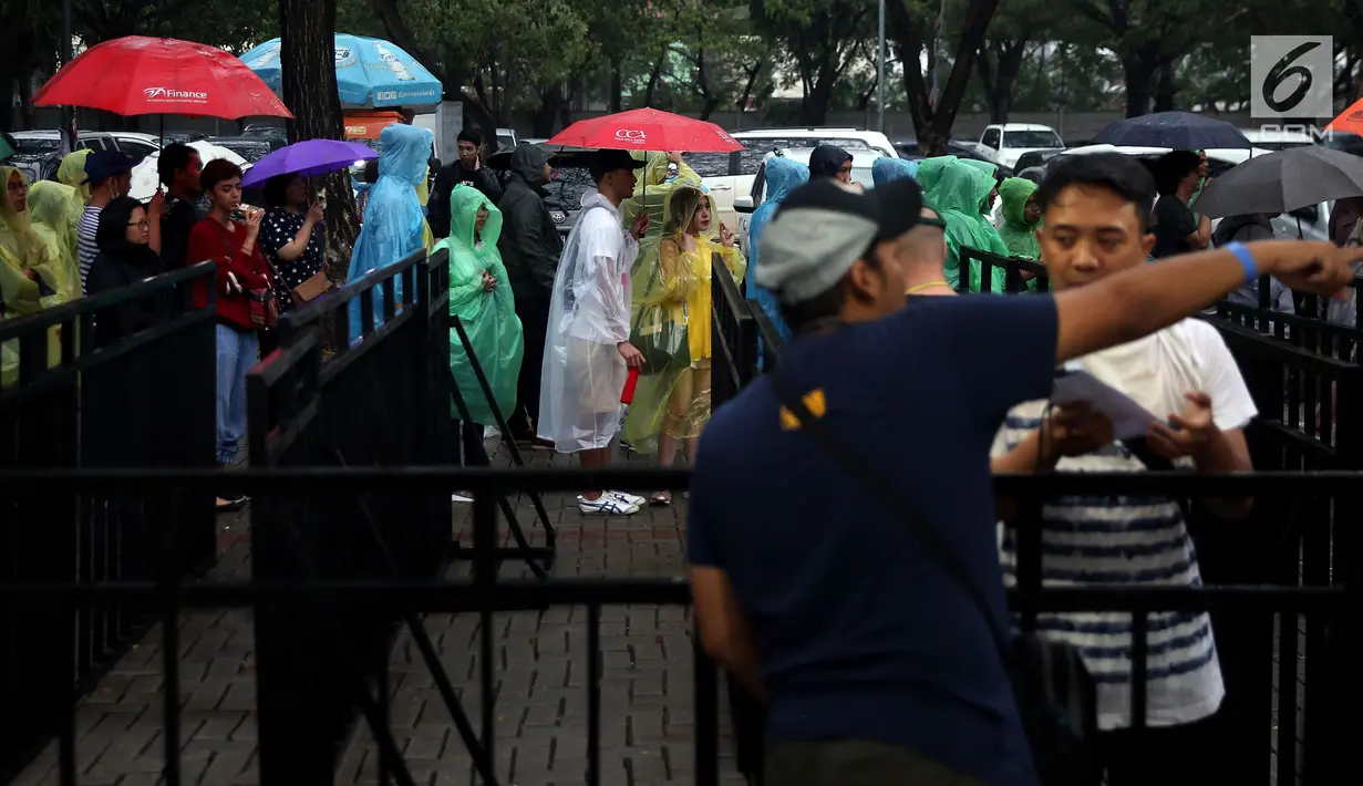 Sepasang muda mudi berteduh jas hujan saat mengantre tiket konser Liam Gallagher di Ecovention Ancol, Jakarta Utara, Minggu (14/1). Ariel NOAH, Rian D'MASIV, hingga Glenn Fredly menyatakan akan menghadiri konser ini. (Liputan6.com/JohanTallo)