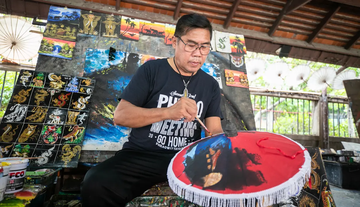 Seorang pengrajin melukis permukaan sebuah payung di Sentra Pembuatan Payung di Desa Bor Sang, Chiang Mai, Thailand, pada 1 November 2020. Desa Bor Sang, sekitar sembilan kilometer di sebelah timur Kota Tua Chiang Mai, terkenal sebagai daerah pembuat payung kertas. (Xinhua/Zhang Keren)