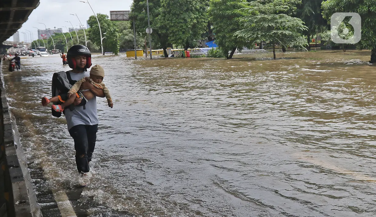 Warga melintasi banjir di Jalan Ahmad Yani, Cempaka Putih, Jakarta, Minggu (23/2/2020). Banjir yang terjadi dari dini hari tadi melumpuhkan akses jalan tersebut. (Liputan6.com/Herman Zakharia)