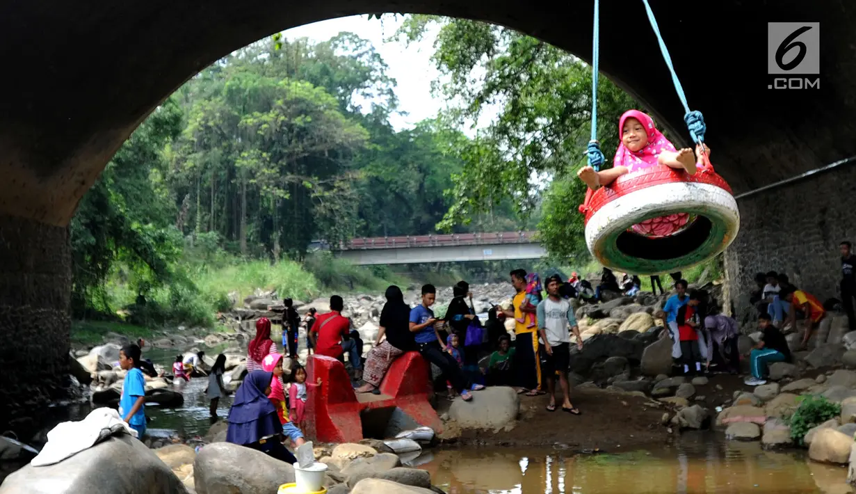 Seorang anak bermain ayunan di kolong jembatan Sempur, Bogor (16/9). Musim kemarau yang menyebabkan debit Sungai Ciliwung menyusut drastis dimanfaatkan warga Bogor dan sekitarnya untuk berwisata murah dan gratis di aliran sungai. (Merdeka.com/Arie Basuki)