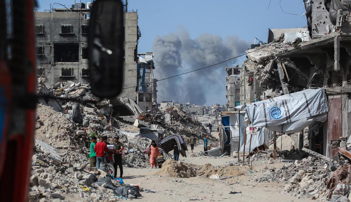 Asap mengepul ke arah utara menjadi latar ketika warga Palestina bergerak melalui Jabalia meninggalkan Jalur Gaza utara menuju Kota Gaza pada 19 Mei 2025. (Bashar TALEB/AFP)