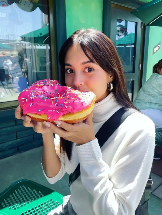 Manisnya penampilan Aurelie Moeremans pakai turtleneck putih, memperlihatkan dirinya sedang menikmati donat yang berukuran sangat besar. [Foto: Instagram/aurelie]