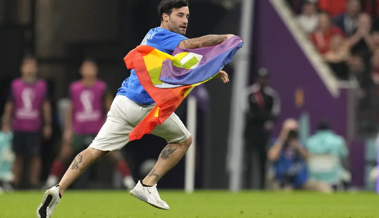 Seorang pria membawa bendera pelangi yang identik dengan LGBT berlari melintasi lapangan selama pertandingan grup H Piala Dunia 2022 Qatar antara Portugal melawan Uruguay di Stadion Lusail di Lusail, Qatar, Senin, 28 November 2022.  Pria itu berada di lapangan selama sekitar 30 detik, sebelum akhirnya dikawal oleh petugas keamanan. (AP Photo/Themba Hadebe)