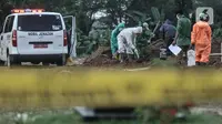 Garis batas polisi terlihat di dekat petugas saat proses pemakaman jenazah korban virus Covid-19 di TPU Tegal Alur, Jakarta, Kamis (25/6/2020). Menurut petugas makam TPU Tegal Alur, selama masa PSBB Transisi jumlah pemakaman jenazah dengan protap Covid-19 meningkat dibanding bulan lalu. (merdeka.com