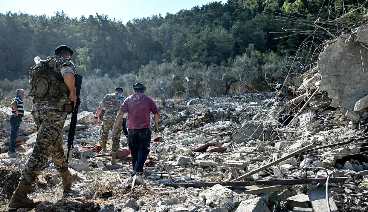Tentara tentara Lebanon dan lainnya berjalan melewati reruntuhan bangunan yang hancur di lokasi serangan udara Israel sebelumnya di desa Aito, Lebanon utara pada 15 Oktober 2024. (JOSEPH EID/AFP)