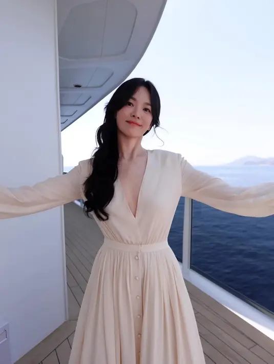 Penampilan paling memikat hadir saat ia berpose di koridor luar kapal dengan latar hamparan laut luas. Mengenakan gaun ivory yang sama, Song Hye Kyo merentangkan kedua tangan sambil memejamkan mata menikmati semilir angin laut. Potret tersebut menghadirkan kesan tenang, bebas, dan sangat elegan tanpa perlu usaha berlebihan. [Dok/@kyo1122].