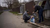Dua pria Ukraina mengisi botol dengan air yang mereka ambil dari air mancur umum di Bucha, di pinggiran Kiev, Ukraina pada Senin (18/4/2022). Warga Bucha masih tanpa listrik, air dan gas setelah lebih dari 43 hari sejak invasi Rusia. (AP Photo/Emilio Morenatti)