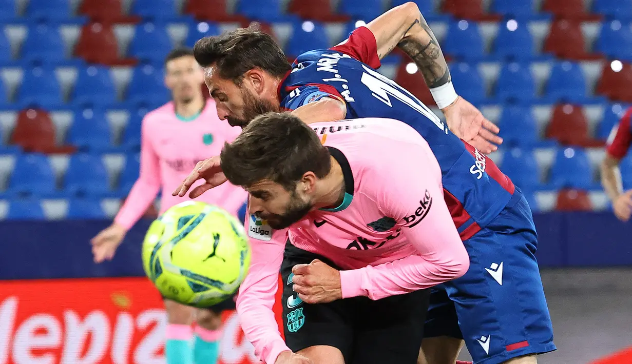 Striker Levante, Enis Bardhi (atas) berebut bola dengan bek Barcelona, Gerard Pique dalam laga lanjutan Liga Spanyol 2020/2021 pekan ke-36 di Ciutat de Valencia Stadium, Valencia, Selasa (11/5/2021). Levante bermain imbang 3-3 dengan Barcelona. (AFP/Jose Jordan)
