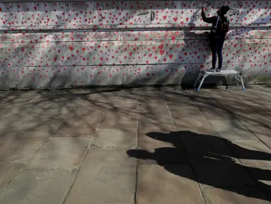 Anggota keluarga yang berduka melukis hati di Dinding Peringatan COVID-19 di seberang Gedung Parlemen Inggris, di London, Senin (29/3/2021). Mural hampir 150.000 lukisan hati tersebut untuk mengenang ribuan orang yang telah meninggal akibat virus corona di Inggris. (AP Photo/Kirsty Wigglesworth)