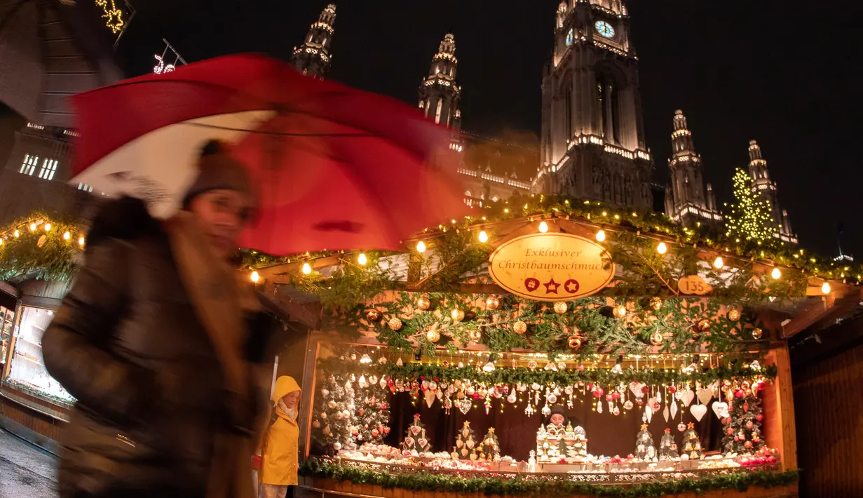 Wisawatan menggunakan payung saat mengunjungi pasar Natal di luar City Hall, Wina pada 26 November 2018. Di Pasar Natal ini, para pengunjung bisa menikmati jajanan khas hingga pernak-pernik kerajinan tangan asli Austria. (JOE KLAMAR / AFP)