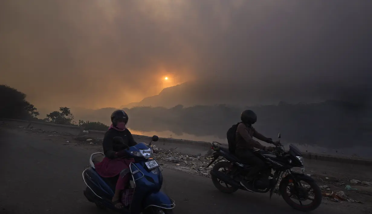 Skuter melintas saat api besar melalap tempat pembuangan sampah Ghazipur di New Delhi, India (28/3/2022). Kebakaran besar terjadi di tempat pembuangan sampah di daerah Ghazipur Delhi timur yang menyebabkan kepulan asap besar menyelimuti wilayah tersebut. (AP Photo/Manish Swarup)