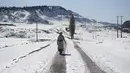 Seorang wanita berjalan pulang di tengah hujan salju lebat di desa Amazigh Timahdite, dikelilingi oleh hujan salju di Atlas Tengah, dekat Azrou, Maroko (4/12/2021). Desa ini berada di ketinggian 1.800 meter (5.900 kaki) di Pegunungan Atlas Tengah. (AP Photo/Mosa'ab Elshamy)