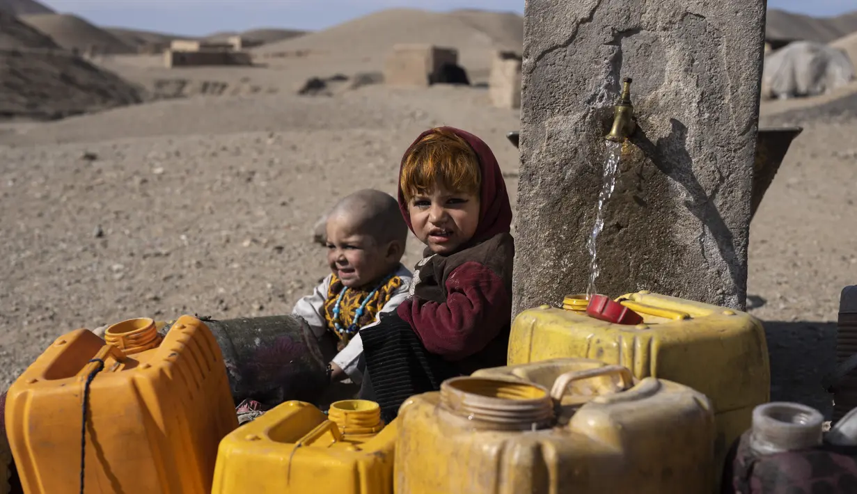 Dua anak Afghanistan duduk di sebelah keran ketika warga desa Kamar Kalagh di luar Herat, mengisi wadah plastik mereka dengan air, pada 26 November 2021. Kekeringan Afghanistan, yang terburuk dalam beberapa dekade, kini memasuki tahun kedua, diperburuk oleh perubahan iklim. (AP/Petros Giannakouris)