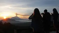 Wisatawan mengambil gambar sambil menikmati matahari terbit (sunrise) di Gunung Agung dari Kintamani, Bali, Rabu (13/12). BNPB menegaskan bahwa kondisi Pulau Bali aman bagi wisatawan meski Gunung Agung berstatus siaga. (AP Photo/Firdia Lisnawati)