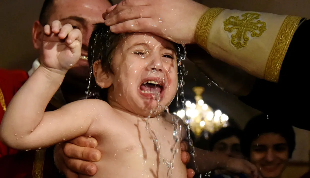 Seorang bayi menangis saat dibaptis dalam upacara pembaptisan massal di Gereja Katedral Holy Trinity, Tbilisi, Georgia (21/1). (AFP Photo/Vano Shlamov)