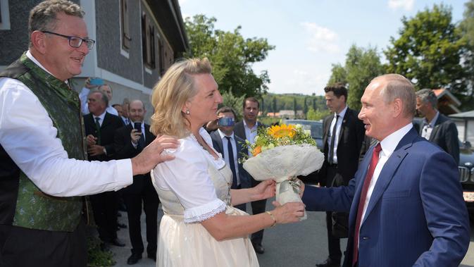 Presiden Rusia, Vladimir Putin memberikan buket bunga saat menghadiri pesta pernikahan Menteri Luar Negeri Austria, Karin Kneissl dengan pengusaha Wolfgang Meilinger di Gamlitz, Sabtu (18/8). (Alexei Druzhinin, Sputnik, Kremlin Pool via AP)