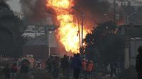 Petugas pemadam dan penyelamat berdiri di dekat kebocoran gas yang terbakar setelah serangkaian ledakan di Puebla, Meksiko, Minggu (31/10/2021). Ledakan besar yang dikaitkan dengan kebocoran gas tersebut merusak puluhan rumah dan menyebabkan sekitar 2.000 orang. (AP Photo/Pablo Spencer)