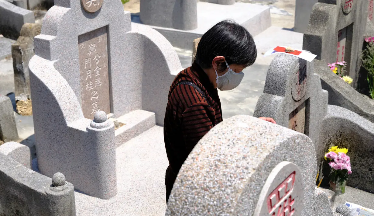 Seorang wanita yang mengenakan masker membersihkan makam kerabat saat Festival Ching Ming atau Hari Sapu Makam di Hong Kong, Selasa (5/4/2022). Ribuan warga Hong Kong memberi hormat kepada leluhur dan kerabat mereka selama festival tahunan ini. (AP Photo/Vincent Yu)
