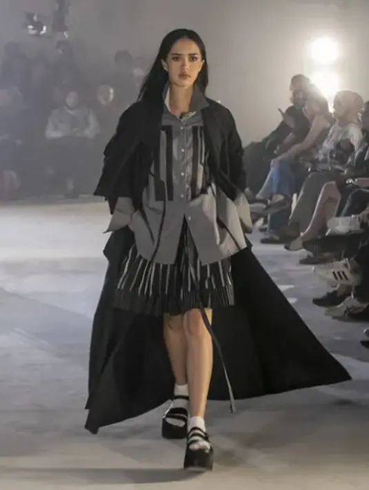 Tampilan kemeja abu-abu berpotongan asimetris, rok rumbai hitam, dan mantel hitam yang serasi. (foto: instagram.com/dsgnsofie)