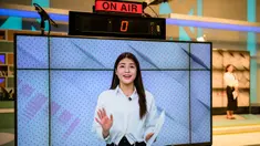 Foto yang diambil di Seoul pada tanggal 17 April 2023 ini menunjukkan seorang aktor manusia (latar belakang-kanan) bersiap untuk menyampaikan laporan saat Zaien, salah satu manusia virtual paling aktif di Korea Selatan yang diciptakan oleh perusahaan Artificial Intelligence Pulse9 terlihat di layar untuk program berita pagi di stasiun televisi Korea Selatan. (ANTHONY WALLACE/AFP)